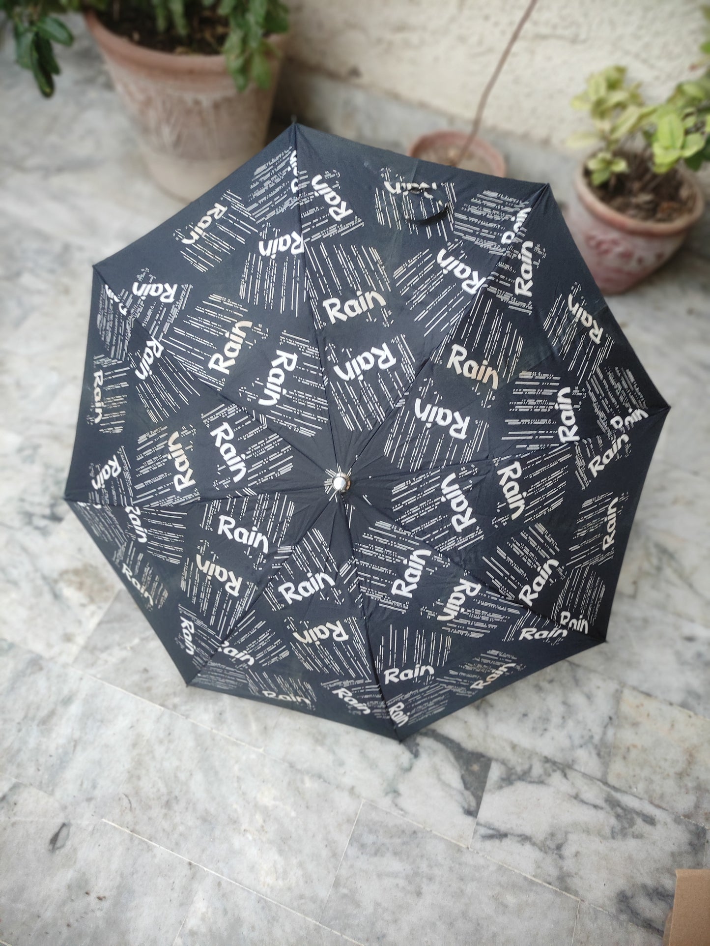 BLACK FOLDING UMBRELLA WITH AN ALL OVER RAIN TEXT PATTERN